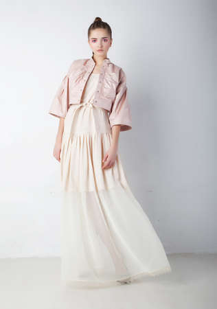 Beautiful attractive supermodel - young woman in elegant fashion dress posing over white wallの写真素材