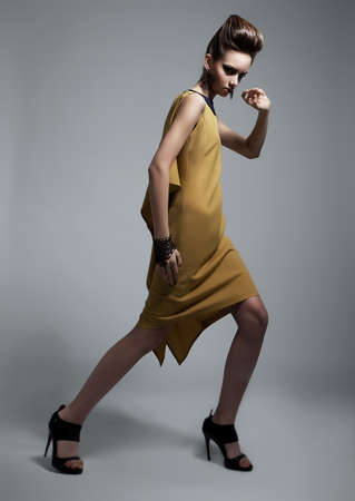 Stylish brunette female wearing yellow fashion dress on gray backgroundの写真素材