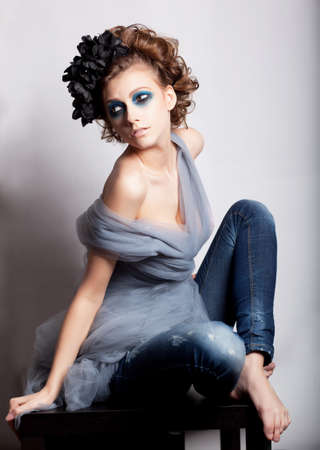Casual beautiful young modern woman with blue make-up sitting in jeansの写真素材