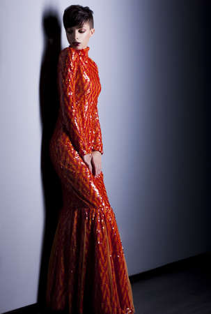 Young fashion woman in trendy red dress posing in studioの写真素材