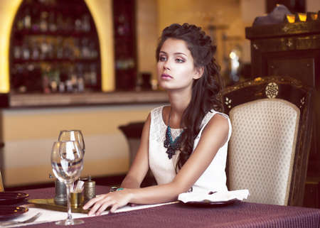 Dating. Dreaming Woman waiting at Decorated Table in Restaurant Interiorの写真素材