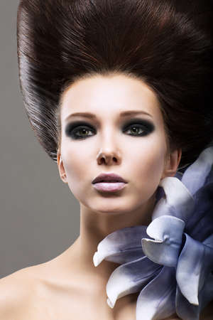 Elegance. Portrait of Young Brunette with Flower. Classy Coiffure and Bright Makeupの写真素材