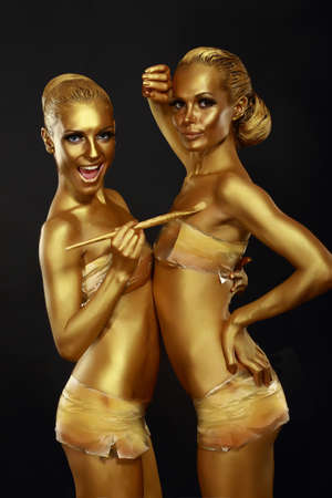 Fancy Dress Party. Couple of Women with Golden Metallic Painted Skin. Creativityの写真素材