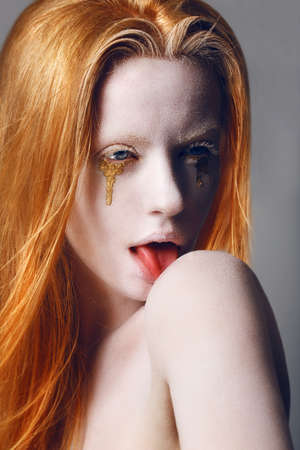 Fantasy. Expression. Eccentric Woman with White Painted Skin and Gold Tears Licking her Shoulderの写真素材