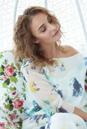 Beautiful woman with closed eyes, smiling. He is sitting in a chair. Bright interior. Flowers.の写真素材