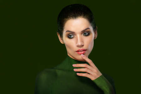 Portrait of a beautiful woman on a green background. Close-up face. think. Thumb near the lips.の写真素材