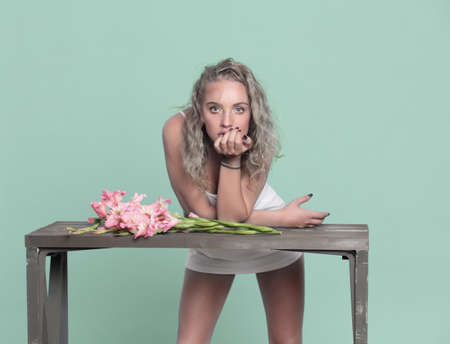 Beautiful female model standing at the table, on the table lay flowers. Green background. Blonde. Style.の写真素材