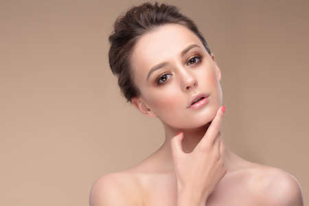 Beige color. Portrait of a woman with natural make-up. Hand near chin.の写真素材