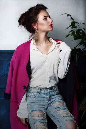 Female model sitting in a crimson coat. Young woman in bright clothes. Fashion, style.の写真素材