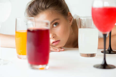 The girl at the white table, looks through the walls with colored drinks.の写真素材