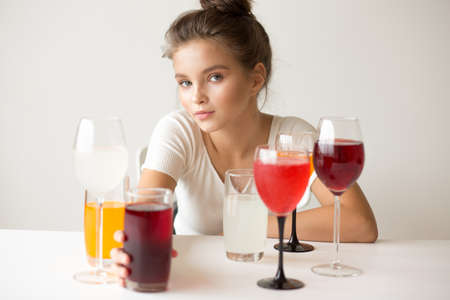 The girl is sitting at the table. Glasses and glasses with multi-colored juices and drinks.の写真素材