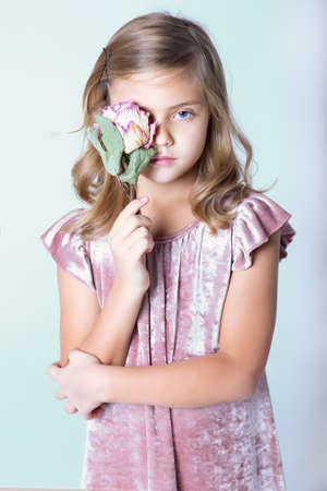 Girl in a pink dress posing in the studio. Closes one eye with a flower.の写真素材