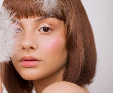 Face close up. Portrait, woman. In the hair and on the face is a white feather. Brown eyes. Bob hairstyle. Clean healthy skin, blush.の写真素材