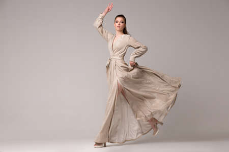 A girl in a long dress posing in the studio in full growth. She runs with her hand up, the ebka of the dress develops and flies.の写真素材