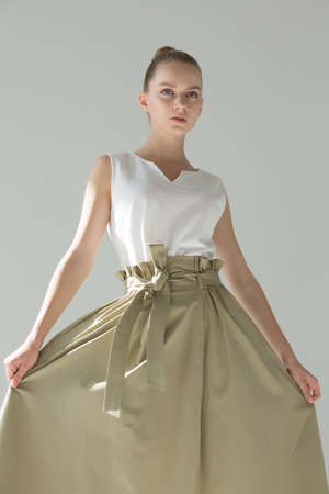 Girl model posing in studio. She holds a wide green skirt in her hands and looks straight. Natural makeup. Wide belt at the waist.の写真素材