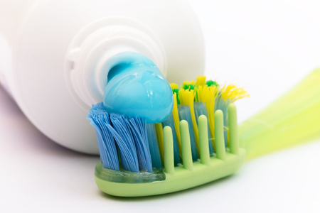 The blue toothpaste on a colored toothbrush coming from the tube. White background. Morning hygiene dental action. Soft focus, focused on the part of toothbrush.の写真素材