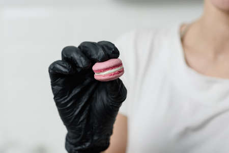 A gloved female hand holding a macaroni cookie or a macaroni dessertの写真素材