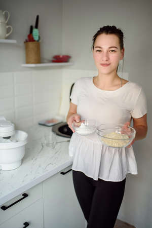 A beautiful woman holds the ingredients for the dough in a glass containerの写真素材
