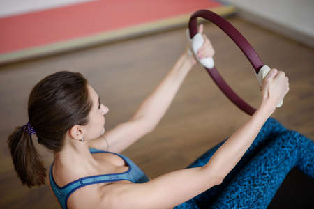 In the gym, a young woman in sportswear clutches a pilates ringの写真素材
