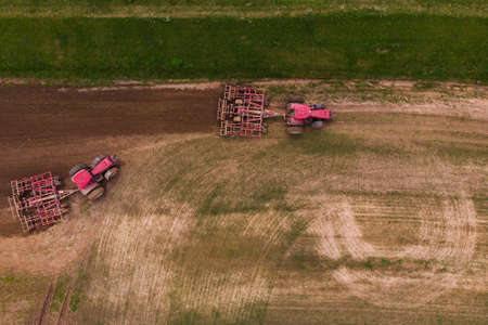 Two tractors with a disc harrow plow the field for sowing. Aerial photography.の写真素材