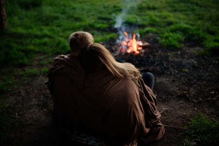A couple in love is sitting, covered with a blanket, and looks at the fireの写真素材