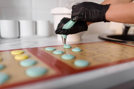 Hands in black gloves squeeze the dough out of a pastry syringe. Making macaroons