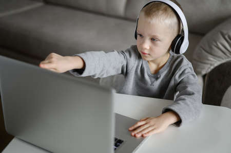 A boy with headphones watches a video tutorial at a PC and performs a taskの写真素材