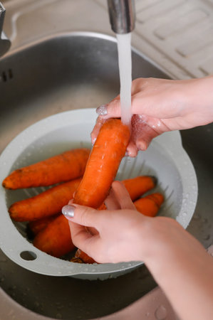 Female hands wash carrots under running water in a colander in the kitchen.The concept of a healthy...