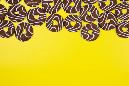 Round chocolate cookies covered with white icing, with a heart carved inside, on a yellow...