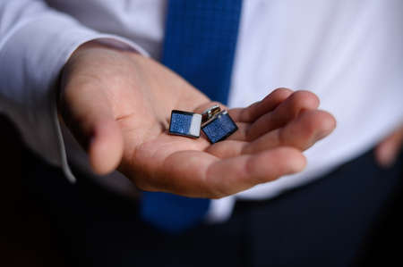 A man in a shirt holds stylish cufflinks in his hands, close-up.の写真素材