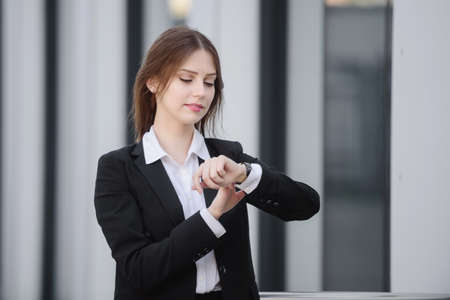 A business woman on the street in a formal suit looks at her wristwatch, checks the time on her watch.の写真素材