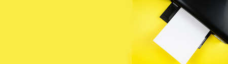 Top view of the printer and a blank sheet of a4 paper on a yellow background.Bannerの写真素材