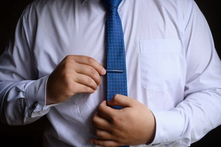 A man in a white shirt puts on and straightens his tie and clip.Wedding day concept, young modern...