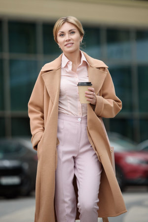 A woman in a business suit walks down the street with a cup of coffee.の写真素材