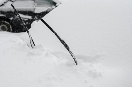 The car is covered with snow after a heavy snowfall, close-up. Car wipers up. Snow cyclone.の写真素材