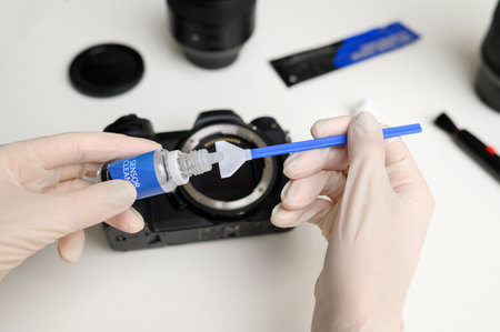 Hands holding sensor cleaning swab and applying a special cleaner to clean the camera sensor. Cleaning and maintaining the mirrorless camera sensor.Care for professional photographic equipment.の写真素材