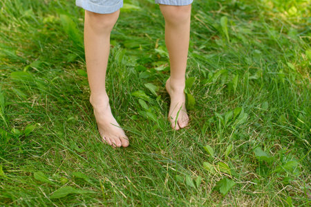 The child walks barefoot on the green grass. The effect of massage on the nerve endings of the legs is the prevention of flat feet in children. The concept of hardening, meditation.の写真素材