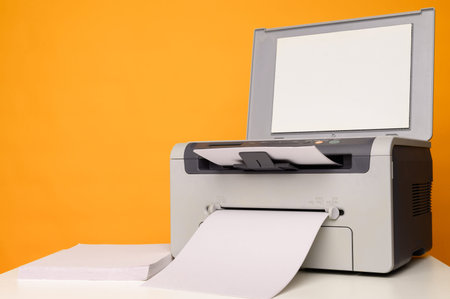 Front view of a multifunction device - printer, copier, scanner and a blank sheet of A4 paper on a...