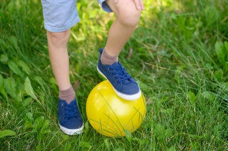 The boy leans his foot on a yellow ball on a sunny summer day, close-upの写真素材
