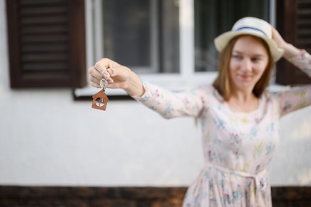 Happy young woman in front of a new house with the keys to a new house, focus on the keys.The concept of real estateの写真素材