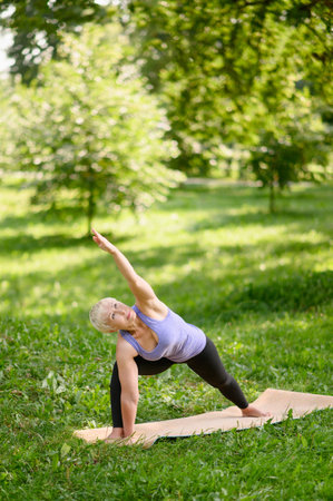 Middle Aged Woman Doing Yoga Outdoors in Extended Triangle Pose.の写真素材