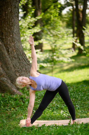 Middle aged woman doing yoga outdoors in extended triangle pose. Copy space.The concept of stretching, Pilates.の写真素材