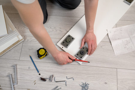 Furniture assembly. The worker installs the legs of the furniture, tightening the screws with a...