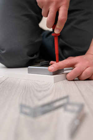 Furniture assembly. The worker installs the legs of the furniture, tightening the screws with a screwdriver.の写真素材