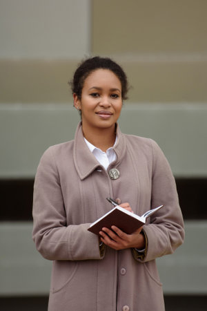 African-american woman in business attire with a notepad conducts an interview against the backdrop of a cityscape.の写真素材