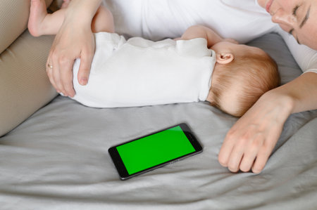 Cute baby and mother hugging sleep at home in bed next to phone, color key. Child safety and protection, co-sleepingの写真素材