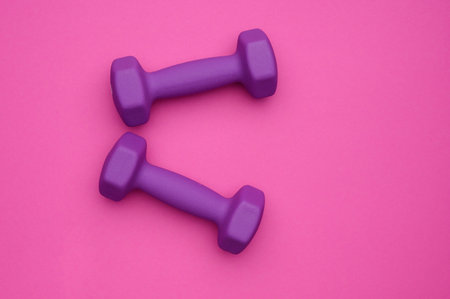 Two rubberized dumbbells of 2 kg of purple color on a pink background. Sports training, fitness,...