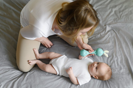 Mom and adorable baby are playing with a rattle. Toy for the development of fine motor skills of the...