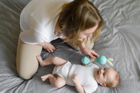 Mom and adorable baby are playing with a rattle. Toy for the development of fine motor skills of the...