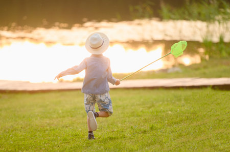 A boy in a hat at sunset plays with scoop-net outdoors on a summer day. Summer outdoor activities for children.の写真素材